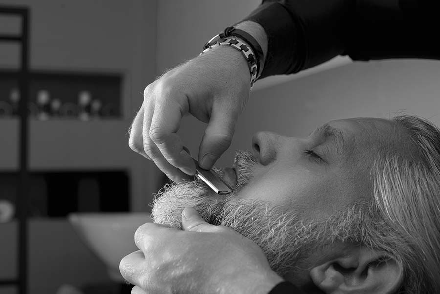 Barber cutting and styling the beard of a gray-haired man.