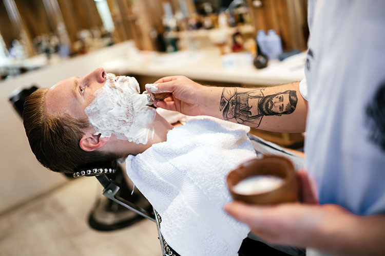 Barber applying beard and mustache treatment to a client's beard during grooming